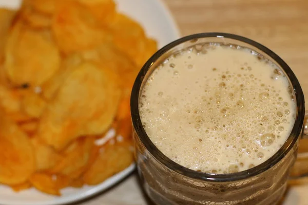 Black beer in big glass cup and tasty chips on white plate