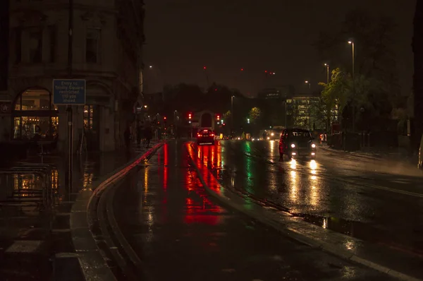 O reflexo do trânsito e luzes nas ruas molhadas de Londres durante a noite com veículos na estrada — Fotografia de Stock