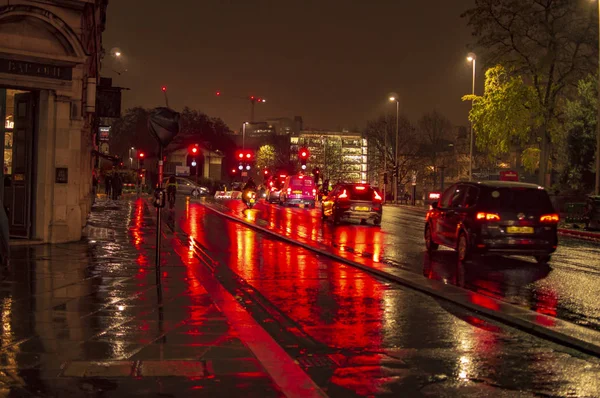 The reflecion of traffic and lights in the wet streets of london during night with red shadow — Stock Photo, Image