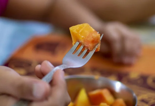 Eating papaya with fork in fingers and the table