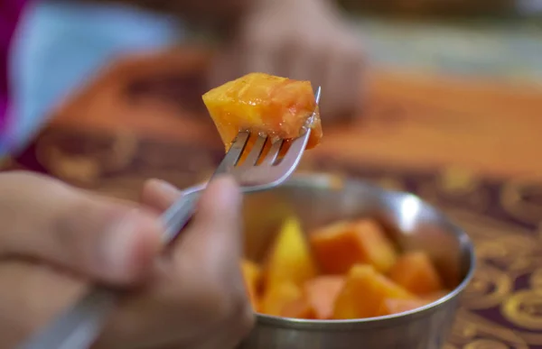 Eating papaya with fork at home with other people