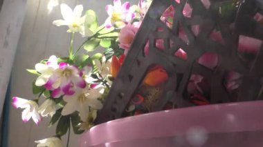 Teras bahçesinde renkli yapay çiçekler ve bir sepet bitki var.