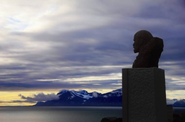 Kuzey Kutbu manzarasının arka planında Lenin anıtının silueti. Karla kaplı uzak engebeli kayalar, Grönland Denizi ve Barentsburg, Spitsbergen Adası, Svalbard, Norveç 'teki dramatik fırtınalı gökyüzü