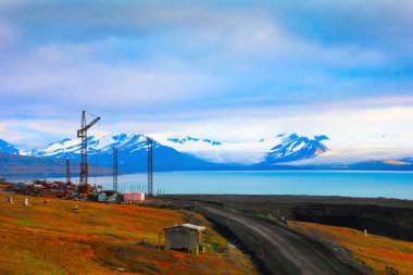 Eriyen kar, çöl yolu ve Barentsburg, Spitsbergen (Svalbard Adası), Norveç ve Grönland yakınlarındaki terk edilmiş vinç ile çorak dağların altındaki mavi körfezin güzel manzarası.