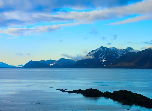 Grönland Denizi 'nin sakin mavi suları ve Spitsbergen' deki (Svalbard Adası) dramatik bulutlu gökyüzünün arka planına karşı uzak sıradağlarla güzel kutup manzarası