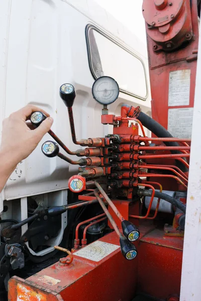 Leverage of rusty red crane truck manually operated hydraulic control  with measuring device and male hand of operator