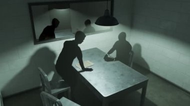 Karanlık siluetleri ile sorgu odası. Dedektif kelepçeli adam sorguluyor