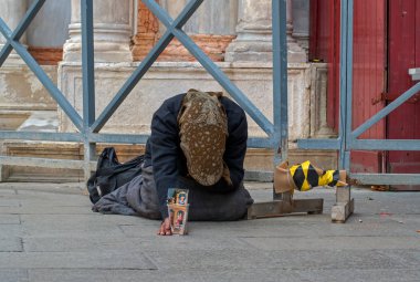 Evsiz bir kadın dilenci sokak Venedik, İtalya için yalvarıyor. Bir kadından bir karton bardak sadaka için onun elinde tutar. Kadın kahverengi bir eşarp, mavi bir ceket ve uzun bir etek giyiyor