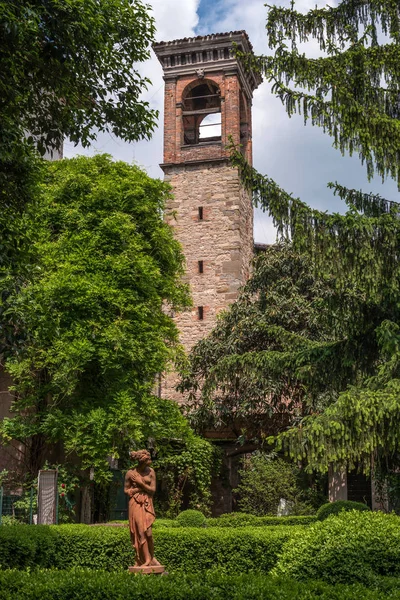 Bergame, Italie - 10 mai 2018 : Vue sur l'ancien clocher, situé dans le feuillage des arbres. Au premier plan se trouve une sculpture de femmes — Photo