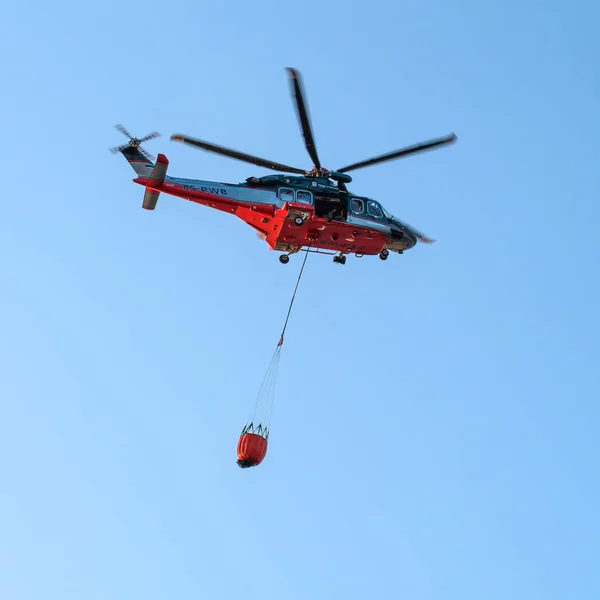 Narva, Estonya - 27 Temmuz 2018: bir helikopter ile kova bir itfaiye yangın hizmet bir ateşi koyarak rol alıyor. Helikopter Agustawestland Aw139 yangın söndürme için donatılmış.
