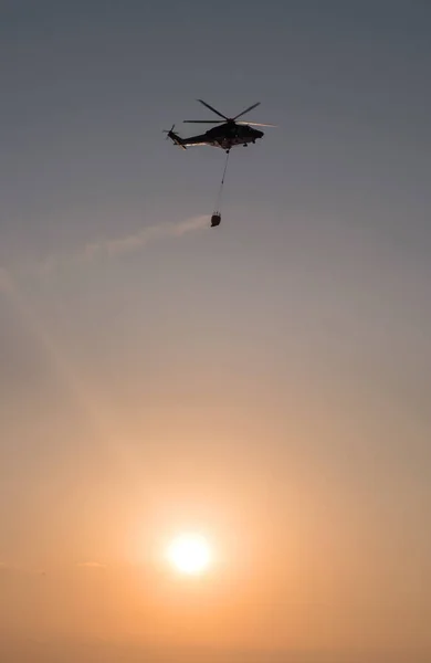 Narva, Estonsko - 27 července 2018: vrtulníku hasiči s požární vědro. Vrtulníku Agustawestland Aw139 vybavena pro boj proti proti zapadajícímu slunci — Stock fotografie