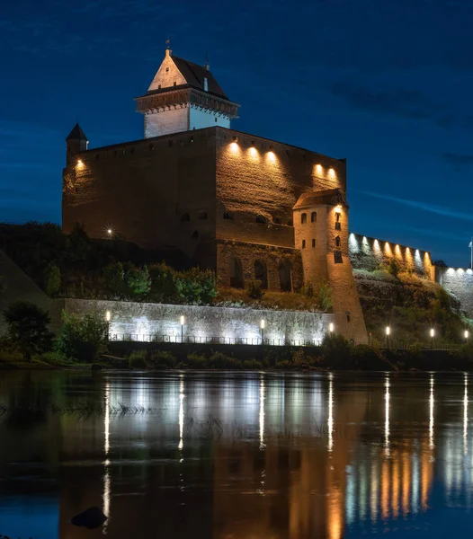 Night view of Narva castle with the tower of High Herman, Narva, Estonia. The castle has a beautiful backlight. The castle is reflected in the water of the Narova River