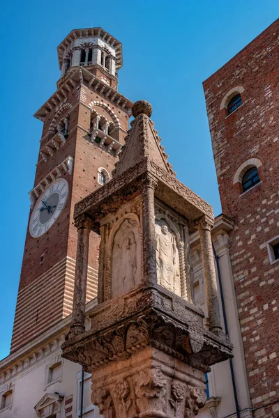 Coluna antiga na praça Erbe em Verona. Na coluna há o brasão de armas da família Visconti e uma imagem de alívio das figuras dos santos. No fundo é a torre Lamberti — Fotografia de Stock