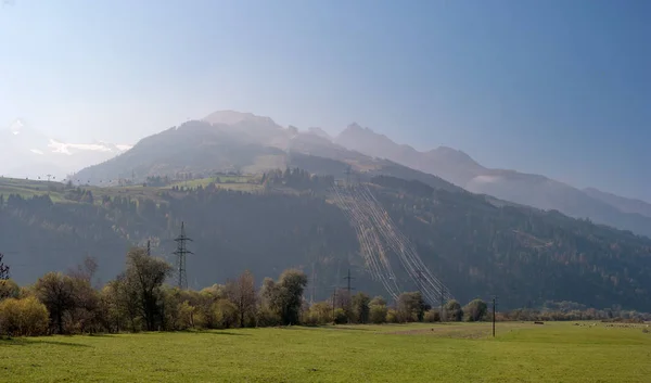 奥地利阿尔卑斯山在早晨 塔楼的电线上有大量的电线离开了这座山 山中的轻雾 在前景的牧场 — 图库照片