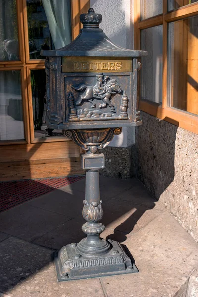 Buzón de metal negro viejo sobre una base de metal. El bajorrelieve se hace en la caja - el cartero en un caballo está tocando un cuerno. El buzón y la base están ricamente decorados . —  Fotos de Stock