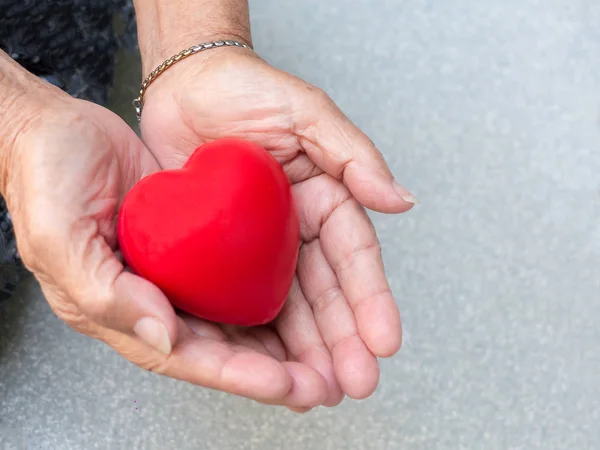 Yaşlı kadınların elinde kırmızı plastik kalp.