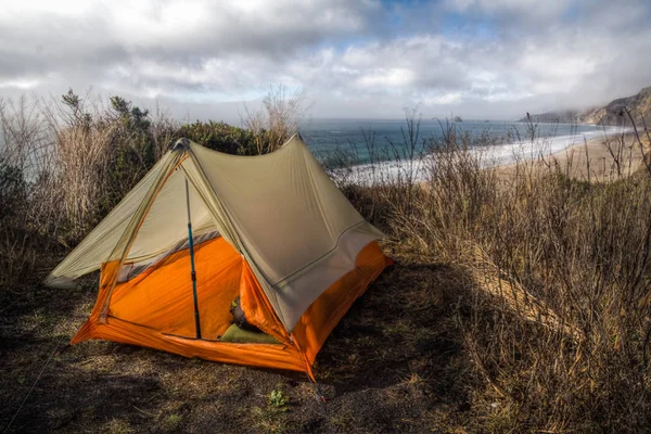 Nice orange tent pitched on cliff overlooking beach and ocean in Point Reyes