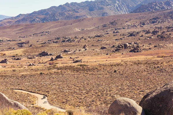 Vehicles drive along a dusty dirt road in the desert of the Buttermilk boulder area of Bishop, California