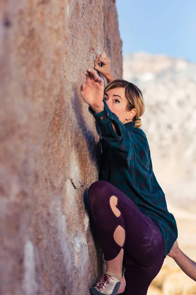 Thin blonde caucasian woman wearing flannel against the cold rock climbing on boulders in the desert of California