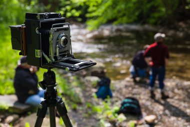 Antique large format camera near a river with people nearby clipart