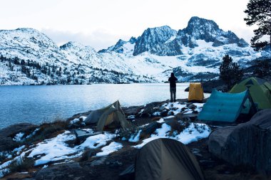 Backpacker and tents on the shore of Garnet Lake at sunset in the Ansel Adams wilderness clipart