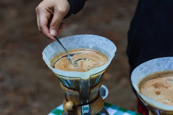 Barista stirs pour over coffee in artisan glass brewer while outdoors