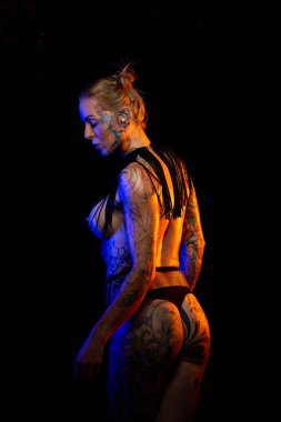 Dövmeli kafkas kadın kaslı ve yağlı deri giyen kolye ve fishnet iç çamaşırı pozlar renkli ışıklar altında