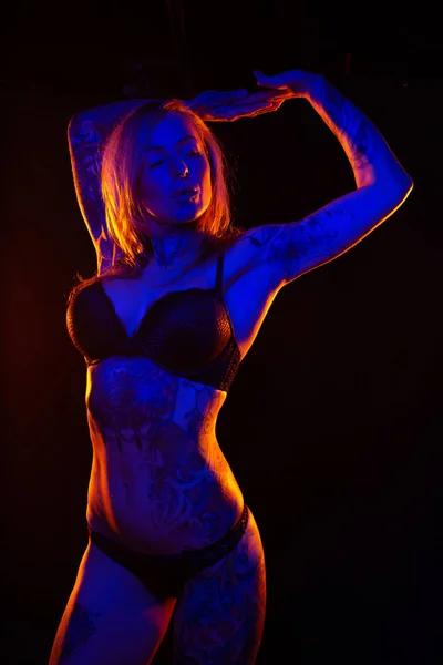 有肌肉的白种人妇女与纹身和涂油皮肤在有色灯下姿势 — 图库照片