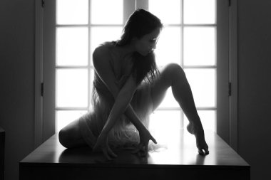 Orta yaşlı beyaz kadın arkadan aydınlatmalı iken bir masada pembe şeffaf elbise teşkil etmektedir