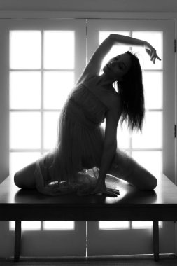 Orta yaşlı beyaz kadın arkadan aydınlatmalı iken bir masada pembe şeffaf elbise teşkil etmektedir