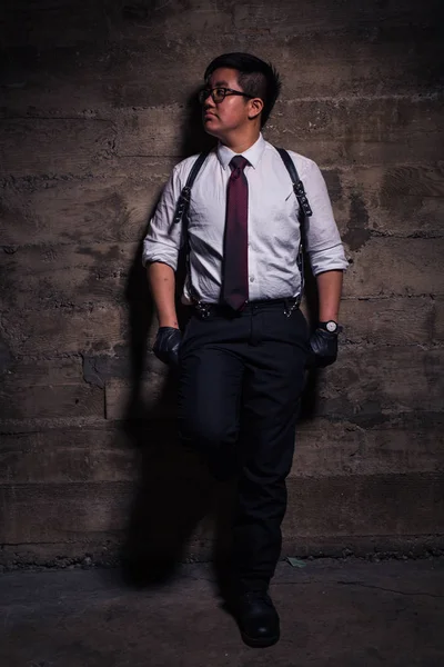Young transgender man in semi formal clothing with a bondage style leather harness poses in a grungy urban location