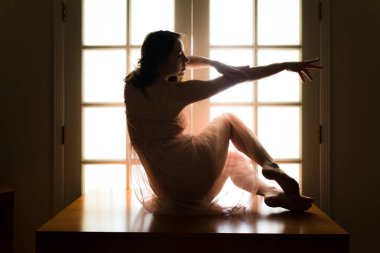 Orta yaşlı beyaz kadın arkadan aydınlatmalı iken bir masada pembe şeffaf elbise teşkil etmektedir