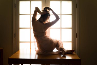 Orta yaşlı beyaz kadın arkadan aydınlatmalı iken bir masada pembe şeffaf elbise teşkil etmektedir