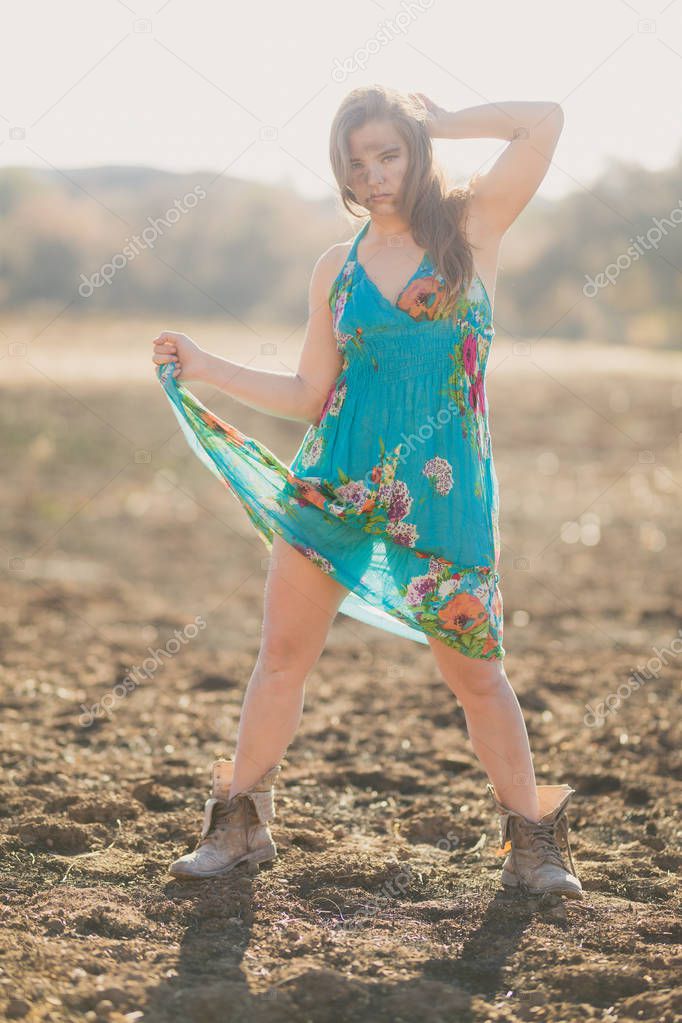 Happy young mixed race woman in blue dress poses in field destroyed by wildfire while covered in ashes