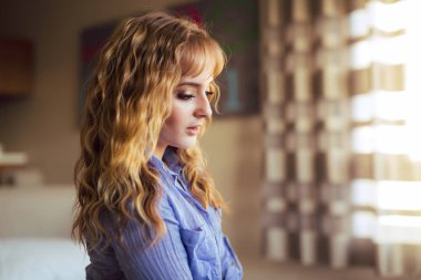 Attactive Genç beyaz bir kadın gözleri iri ve açılarak mavi gömlek ile pencere altın saat ışık ile poz veriyor