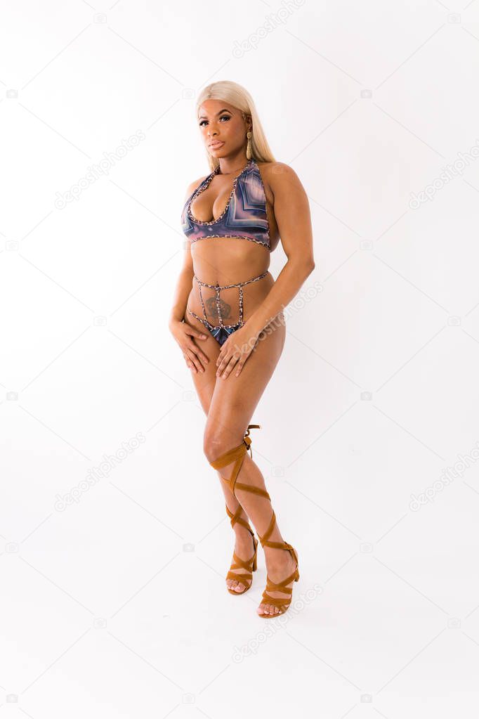 Fit young mixed race woman with long blonde hair poses in a striped blue two piece with tall strappy leather boots against a white background