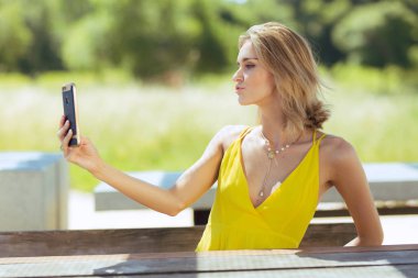 Büyük smartphone açık havada kullanarak ince sarı güneşin içinde çekici genç sarışın beyaz kadın