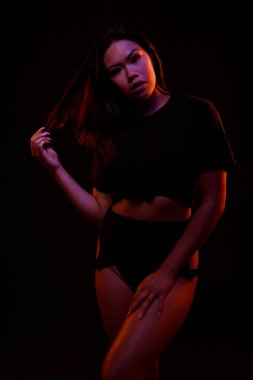 Turuncu ve mavi renkli ışıklar altında siyah karşı uygun Genç Asyalı kadın siyah tek parça pozlar