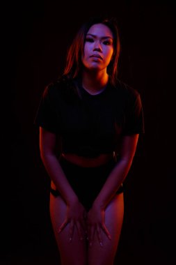 Turuncu ve mavi renkli ışıklar altında siyah karşı uygun Genç Asyalı kadın siyah tek parça pozlar