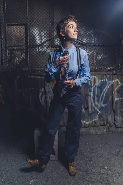 Queer woman dressed in suit and tie poses in a grungy industrial location