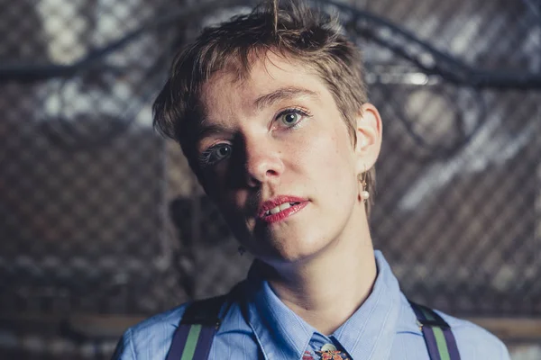 Queer woman dressed in suit and tie poses in a grungy industrial location