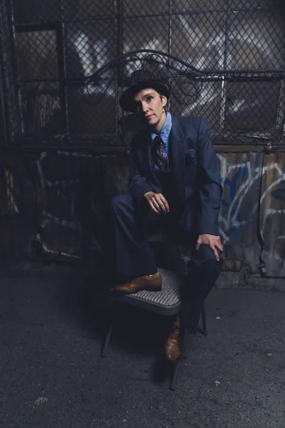 Queer woman dressed in suit and tie poses in a grungy industrial location