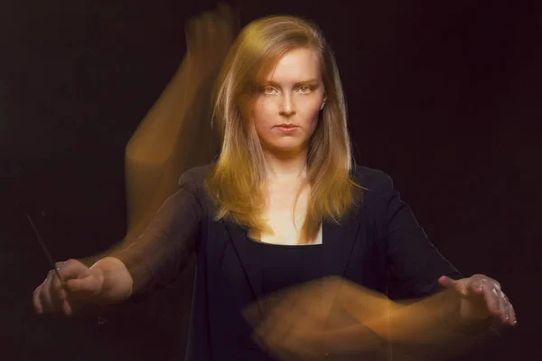 Young caucasian woman conductor gestures with baton and leaves light trails