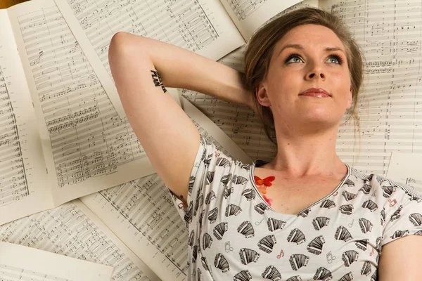 Young caucasian hipster woman with music shirt lies on sheet music in a room