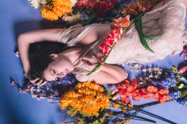 Genç kafkas kadın çiçek mavi bir arka plan karşı yığını yatıyor. Saf beyaz elbise