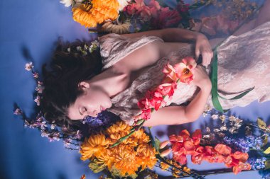 Genç kafkas kadın çiçek mavi bir arka plan karşı yığını yatıyor. Saf beyaz elbise