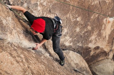 Kırmızı şapkalı, güneş gözlüklü beyaz bir kadın çöle tırmanıyor.