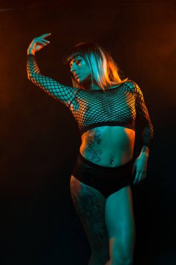 Bangs ve renkli saç ile alternatif model bir fishnet üst giyen teal ve turuncu ışık altında pozlar