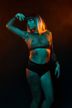 Bangs ve renkli saç ile alternatif model bir fishnet üst giyen teal ve turuncu ışık altında pozlar