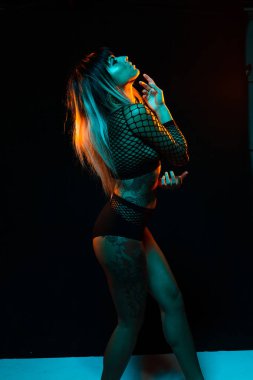 Bangs ve renkli saç ile alternatif model bir fishnet üst giyen teal ve turuncu ışık altında pozlar